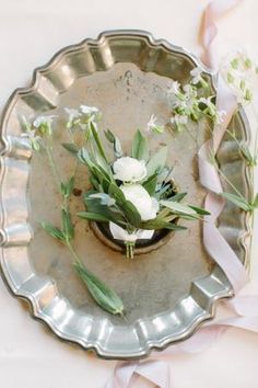 flowers are placed in a silver bowl on a white tablecloth with pink ribbon around it