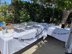 the table is set up for an outdoor party with white linens and blue streamers