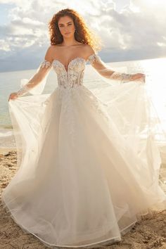 a woman standing on top of a sandy beach wearing a wedding dress with long sleeves