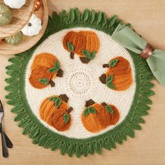 a crocheted placemat with pumpkins on it next to utensils