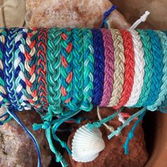 there are many bracelets in the bowl on the table next to some rocks and seashell