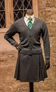 a mannequin dressed in a skirt and sweater stands next to a stone building