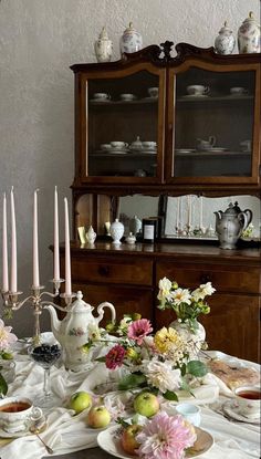 a dining room table with plates, cups and flowers on it in front of a china cabinet