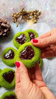 a person is holding some green cookies with jam on them and other decorations in the background