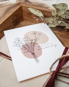 a card with some flowers on it sitting in a wooden box next to a plant