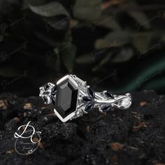 a black diamond ring sitting on top of a rock next to a plant with leaves