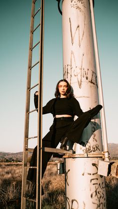 a woman sitting on top of a metal ladder next to a tall white pole with graffiti written on it