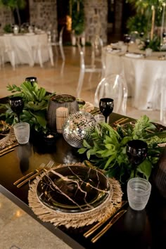 the table is set with black and white plates, silverware, and greenery