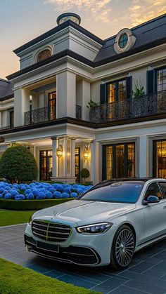 a white car is parked in front of a large house with blue flowers and bushes