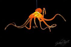 an orange octopus lamp hanging from a string on a black background with the light turned on