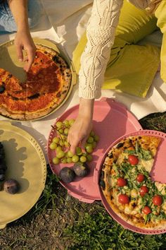 a person cutting a pizza with olives and tomatoes on the table next to other plates