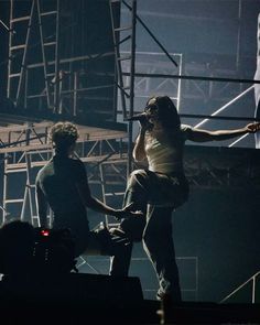 a man standing on top of a stage while holding a microphone to his ear as another man stands next to him