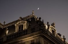 the moon is shining brightly in the sky above an old building with statues on it