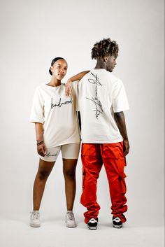 two people standing next to each other wearing white shirts and red pants with writing on them