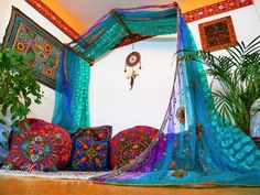 a bed covered in lots of colorful pillows next to a potted plant and wall hanging