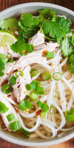 a white bowl filled with noodles and meat topped with cilantro, green onions and garnishes