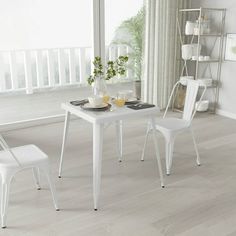 a white dining table with two chairs next to it and a plant on the side