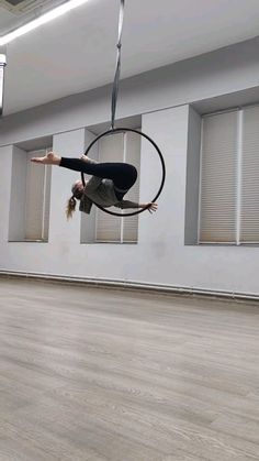 a woman hanging upside down on a hoop in an empty room with windows and blinds