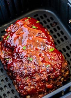 a meatloaf covered in sauce and green onions on top of an air fryer