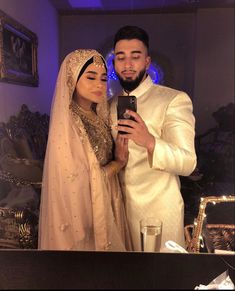 a man and woman standing next to each other in front of a table holding a cell phone