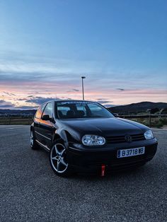 a black car parked in a parking lot with the sun setting behind it and mountains in the distance