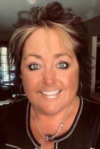 a woman with blue eyes is smiling for the camera while wearing a black shirt and silver necklace