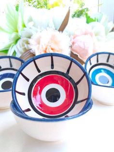 three bowls with eyes painted on them and flowers in the background