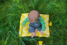 a baby sitting on top of a yellow and white blanket in the grass next to flowers