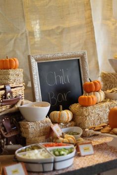 a table topped with hay bales filled with different types of foods and vegetables next to a chalkboard sign