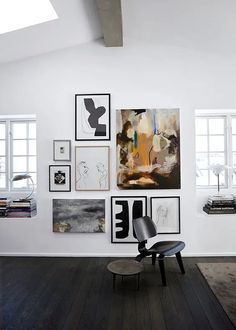 a white room with black and white artwork on the wall, an eames chair and bookshelf