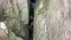 two people are standing in the middle of some large rocks with moss growing on them