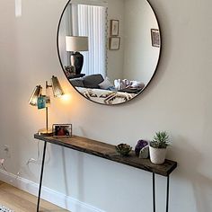 a mirror is hanging on the wall above a table with a lamp and potted plant