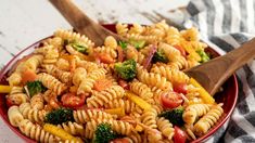 a red bowl filled with pasta and veggies next to a wooden spatula