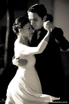 a bride and groom dance together at their wedding reception in black and white, with one holding his arm around the other's neck