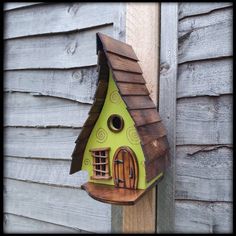 a green birdhouse on the side of a wooden fence