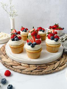 cupcakes topped with fresh berries and whipped cream are on a platter next to other desserts