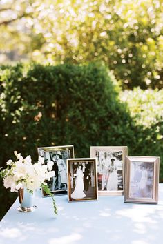 a table topped with pictures and flowers on top of white cloth covered tables in front of trees