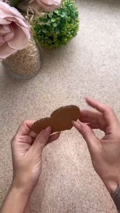 two hands are holding a piece of cookie on the table next to some pink flowers