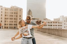 a man and woman standing on top of a roof with buildings in the back ground