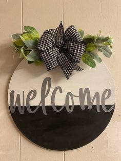 a welcome sign hanging on the side of a wall with a bow and greenery