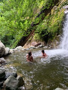 two people are in the water near a waterfall