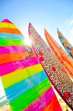 colorful surfboards are lined up on the beach in front of the sun and blue sky