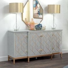 a white and gold sideboard with two lamps on it next to a wall mounted mirror