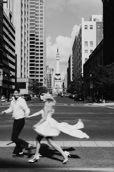 black and white photograph of two people dancing in the street with tall buildings behind them