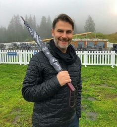 a man holding an umbrella in front of a white picket fence and green grass field