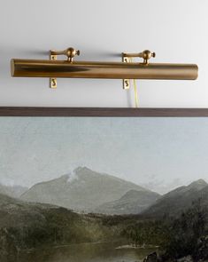 a painting is hanging on the wall above a framed photo with two brass handles, and there are mountains in the background