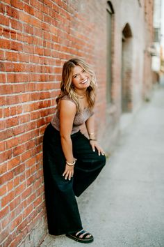 a woman leaning against a brick wall