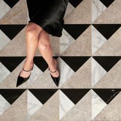 a woman's legs in high heels standing on a marble floor with black and white tiles