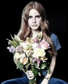 a woman with long hair holding a bouquet of flowers in front of her face and sitting on the floor