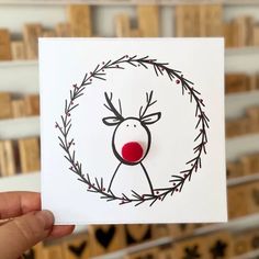 a hand holding up a card with a reindeer on it's face and red nose